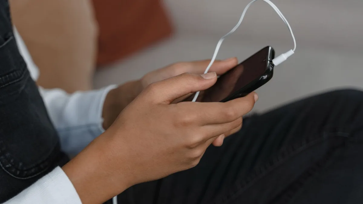 Bir kullanıcı kablosuz kulaklıkla akıllı telefonundan sesli içerik dinliyor.