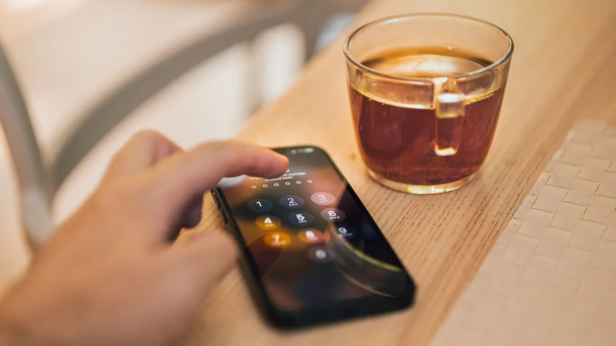 Bir kişinin telefon ekranına PIN kodu girmeye çalışırken parmağının yakın çekim görüntüsü